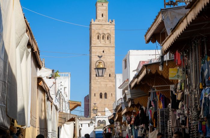 A bustling souk in the Marrakech medina with the Koutoubia minaret in the background